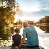Grandfather-and-grandson-sitting-on-a-dock-by-a-lake-watching-beautiful-sunset,-bonding,-enjoying-nature-together-2178445027_6720x4480-resized