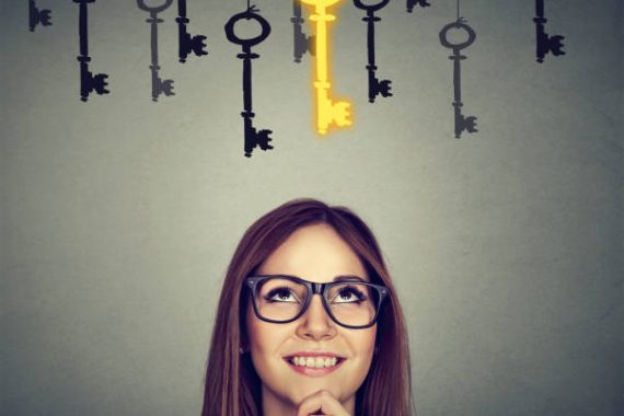 Beautiful thoughtful woman looking upSmiling woman looking up at vintage golden key to success among many others hanging. Concept of business aspirations, achievement
